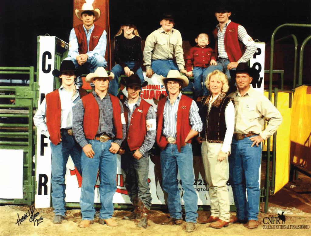 Team photo of the Fort Scott Community College rodeo squad at the College National Finals Rodeo. The CNFR College National Finals Rodeo logo is at the bottom right, with livestock panels, dirt arena flooring, and bright lighting completing the indoor rodeo setting.