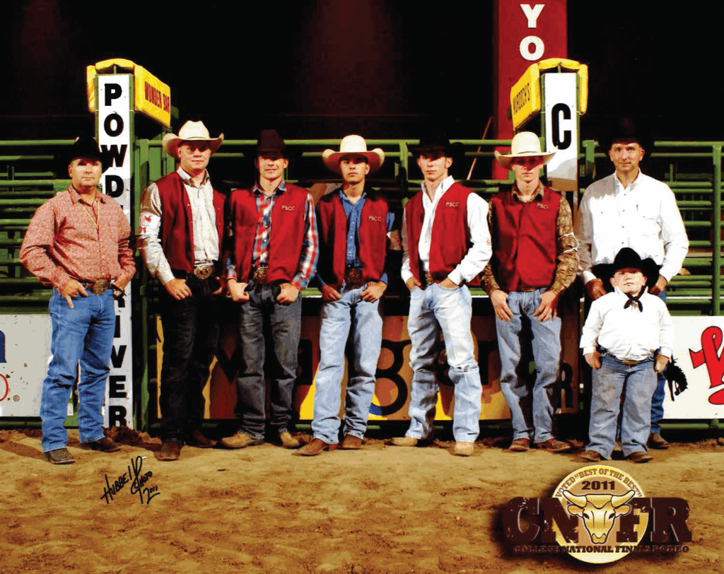 Group photo of eight Fort Scott Community College rodeo team members in an indoor arena at the College National Finals Rodeo 2011. FSix young men wearing cowboy hats and FSCC vests stand in front of yellow-and-brown chutes labeled 'Powder River' and 'Y-O C.' Two others—one man in a white shirt and a young boy in a western outfit—stand at the far right. All are dressed in western attire, with jeans, boots, cowboy hats or belts. The 2011 College National Finals Rodeo logo is at the bottom right, with green arena railings and overhead lights in the background.