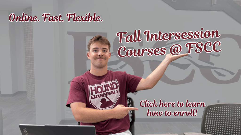 Fall Intersession Image shows a student sitting at a desk in a modern school lobby area. The student wears a maroon "Hound Baseball" t-shirt and points with both hands to large, stylized maroon text overlaid on the right: "Fall Intersession Courses @ FSCC." At the top left, maroon script reads "Online. Fast. Flexible." In the lower right, more maroon text says "Click here to learn how to enroll!" The student's face is blurred for privacy, and the faint background features a large FSCC Greyhounds logo mural on the wall, surrounded by modern decor, computer, and chairs.